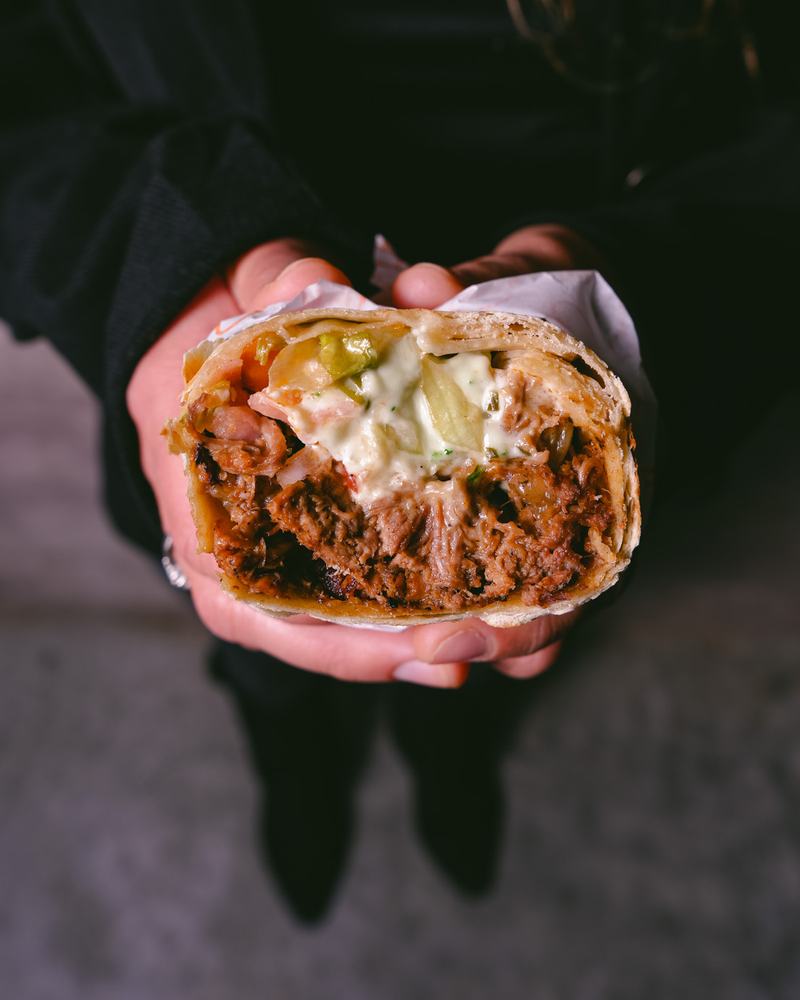 Wrap de carne con salsa cremosa sostenido con las dos manos, producto de Baladi