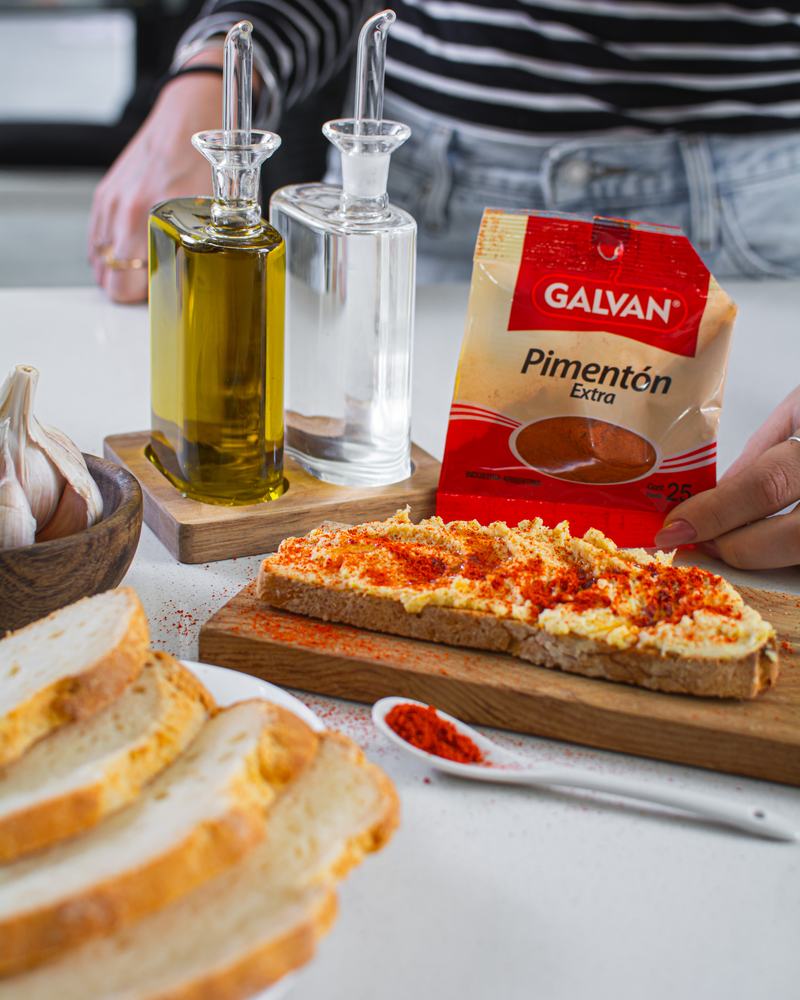 Tostada con pimentón extra Galvan, aceite de oliva y ajo sobre una tabla de madera, producto de Galvan