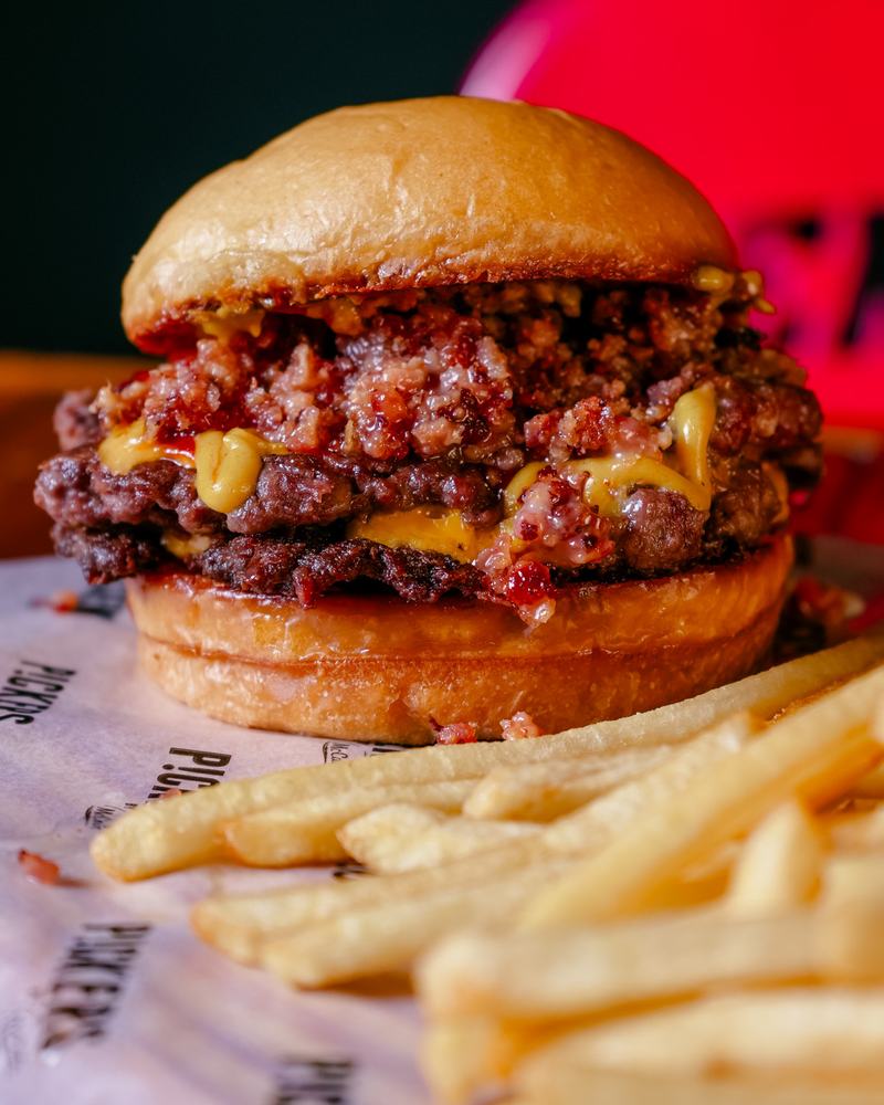 Hamburguesa doble con panceta crocante, cheddar y mostaza junto a papas fritas, producto de Hendrix