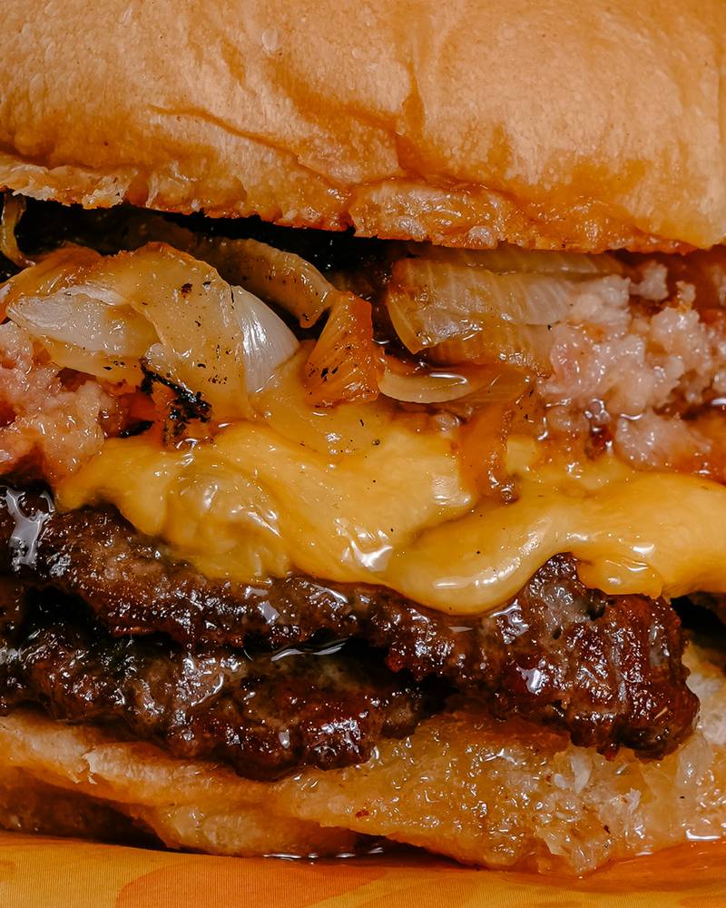 Primer plano de una hamburguesa doble con cheddar, cebolla caramelizada y panceta, producto de Hendrix