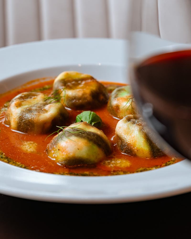 Pastas rellenas con salsa de tomate y pesto, junto a una copa de vino tinto, producto de Pasta Lover's