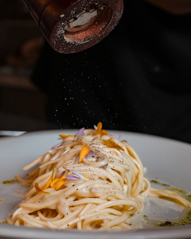 Espagueti en salsa cremosa con flores comestibles y pimienta recién molida, producto de Pasta Lover's