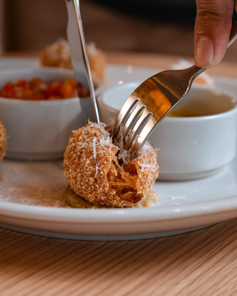 Bocado frito rebozado con queso rallado, abierto con tenedor y cuchillo, junto a dos salsas, producto de Pasta Lover's
